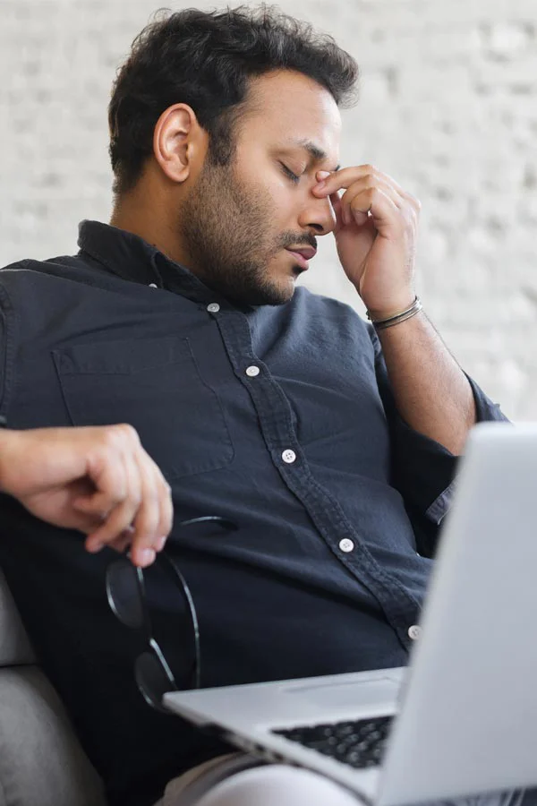 Adrenal-Fatigue-Treatment A middle-aged man with a laptop closing his eyes and rubbing his nose. He needs treatment for Adrenal Fatigue Syndrome from Frank Lanzisera, D.C. in Tampa Bay Metro.