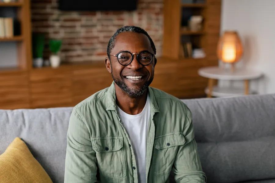 Andropause-Doctor A middle aged black man in a green button up shirt sits on his couch smiling, happy with his treatment for andropause and low testosterone from Frank Lanzisera, D.C. in Tampa Bay Metro.
