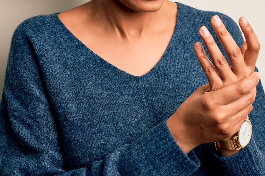Arthritis-Doctor Close up of a woman in a blue sweater massaging one aching hand with the other. Get help for arthritis from Frank Lanzisera, D.C. in Tampa Bay Metro.