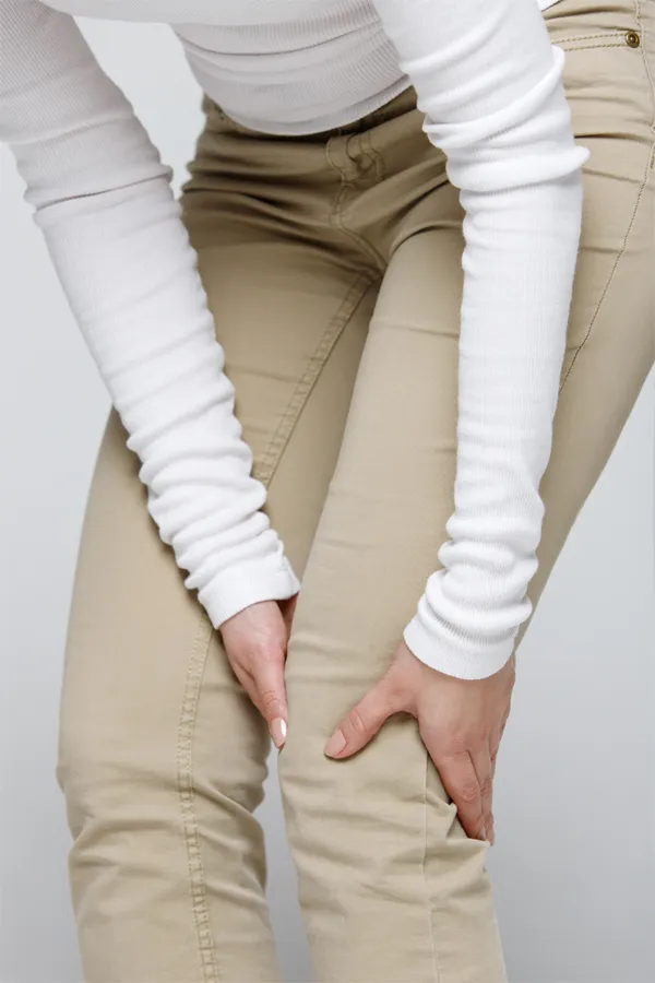 Arthritis-Treatment A woman wearing a white long-sleeve shirt and tan pants, clutching her knee, suffering from arthritis. Get arthritis treatment from Frank Lanzisera, D.C. in Tampa Bay Metro.