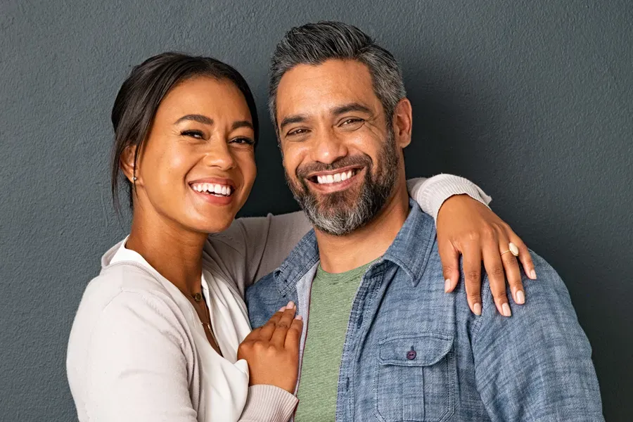 Bioidentical-Hormone-Therapy-Doctor A middle-aged couple with their arms around each other standing against a gray background and smiling, happy with the bioidentical hormone therapy they received from Frank Lanzisera, D.C. in Tampa Bay Metro.