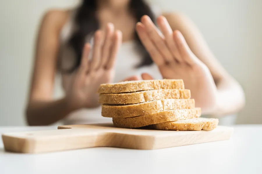 Celiac-Disease-Clinic Close up of a stack of bread slices on a cutting board with a woman's hands behind them, refusing to eat. Get treatment for Celiac Disease from Frank Lanzisera, D.C. in Tampa Bay Metro.