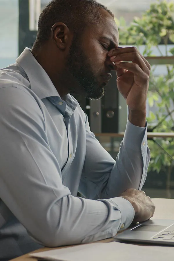 Chronic-Fatigue-Treatment A black man rubbing the top of his nose at his desk, in need of chronic fatigue treatment from Frank Lanzisera, D.C. in Tampa Bay Metro.