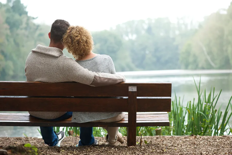 Functional-Medicine-Doctor A couple wearing sweaters seen from behind sitting on a bench and looking out at a relaxing lake and forest, representing functional medicine treatment from Frank Lanzisera, D.C. in Tampa Bay Metro.