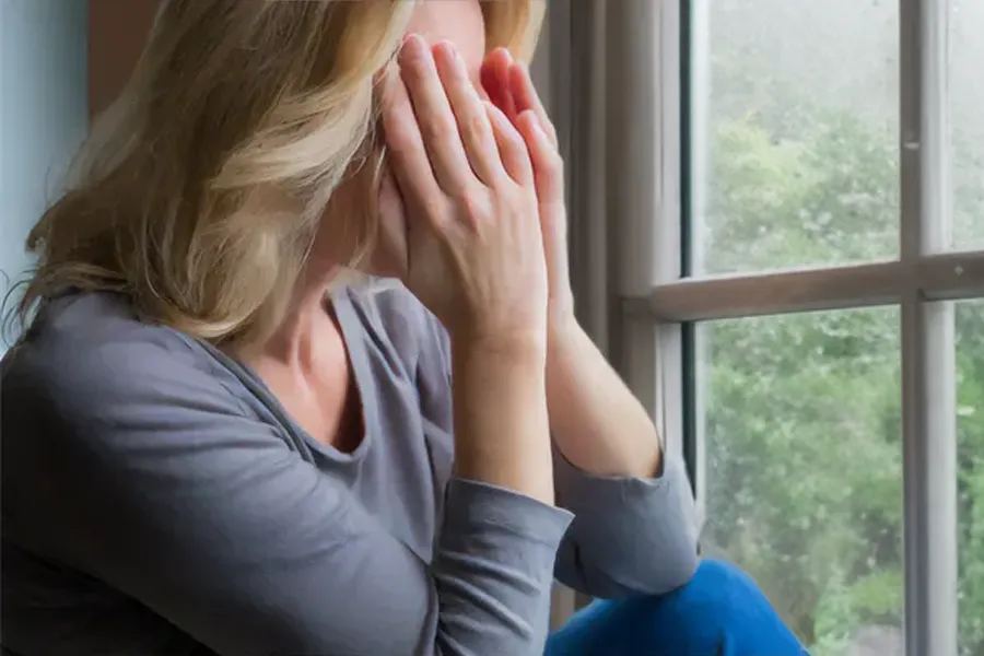 Graves-Disease-Clinic A blonde woman in a gray shirt sits in front of a window on a rainy day covering her eyes with her hands. Get treatment for Grave's Disease from Frank Lanzisera, D.C. in Tampa Bay Metro.