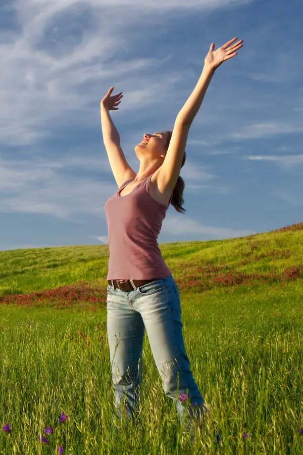 Graves-Disease-Treatment A woman in a tank top and jeans looks up with her arms outstretched to the sky in a field after successful treatment for Grave's Disease from Frank Lanzisera, D.C. in Tampa Bay Metro.