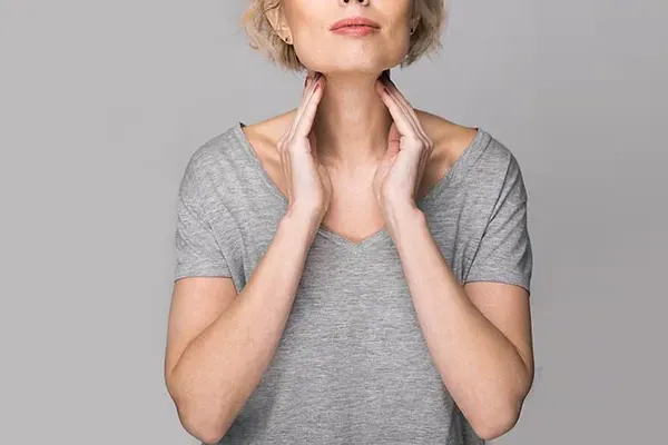 Hashimotos-Thyroiditis-Doctor An older blonde woman in a gray t-shirt holds her hands to her neck checking for signs of thyroid problems. Get help for Hashimoto's Thyroiditis from Frank Lanzisera, D.C. in Tampa Bay Metro.