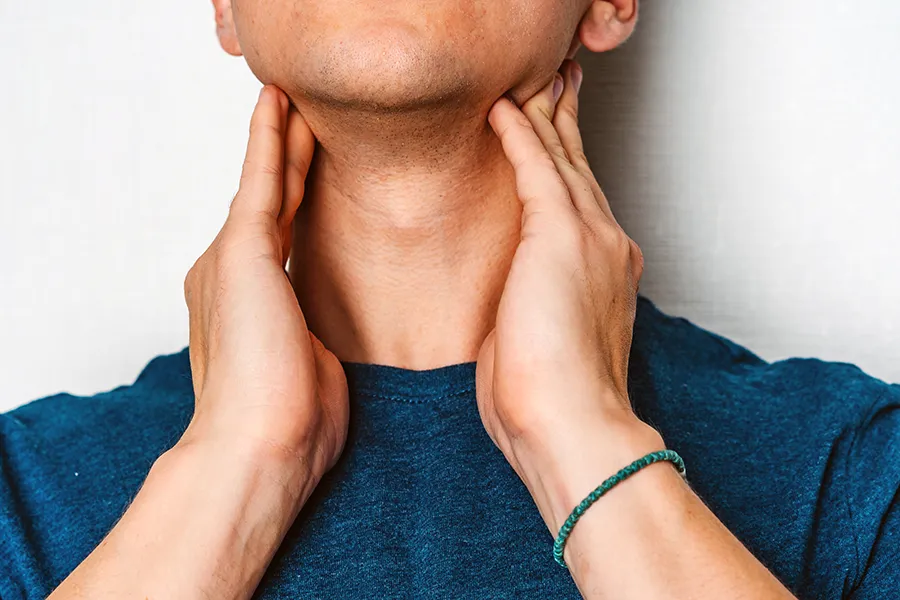 Hypothyroidism-Clinic A man in a dark teal shirt rubs the lymph nodes on his neck. Get hypothyroidism treatment from Frank Lanzisera, D.C. in Tampa Bay Metro.