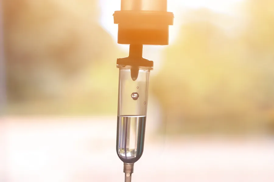 IV-Therapy-Doctor Close-up of an IV drip warmly lit by a window showing trees and a sunset, representing IV therapy from Frank Lanzisera, D.C. in Tampa Bay Metro.