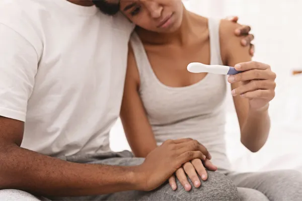 Infertility-Clinic A black couple sits on a bed, disappointed with the negative results of a pregnancy test. Get treatment for infertility from Frank Lanzisera, D.C. in Tampa Bay Metro.