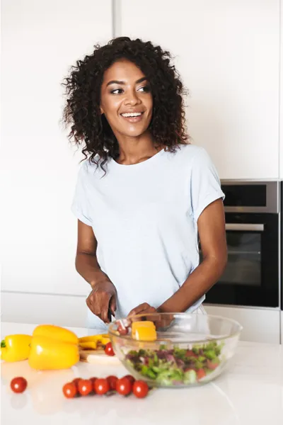 Irritable-Bowel-Syndrome-Treatment Image featuring a smiling woman chopping vegetables for a salad in a bright, white kitchen. Frank Lanzisera, D.C. offers Irritable Bowel Syndrome Treatment and Digestive Support in Tampa Bay Metro.