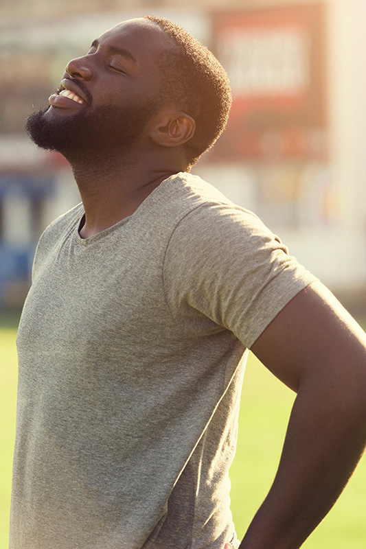 Lean-Muscle-and-Recovery-Treatment A black man in a gray t-shirt and smiles, looking up with closed eyes after a satisfying workout. Get treatment for lean muscle loss and recovery from Frank Lanzisera, D.C. in Tampa Bay Metro.