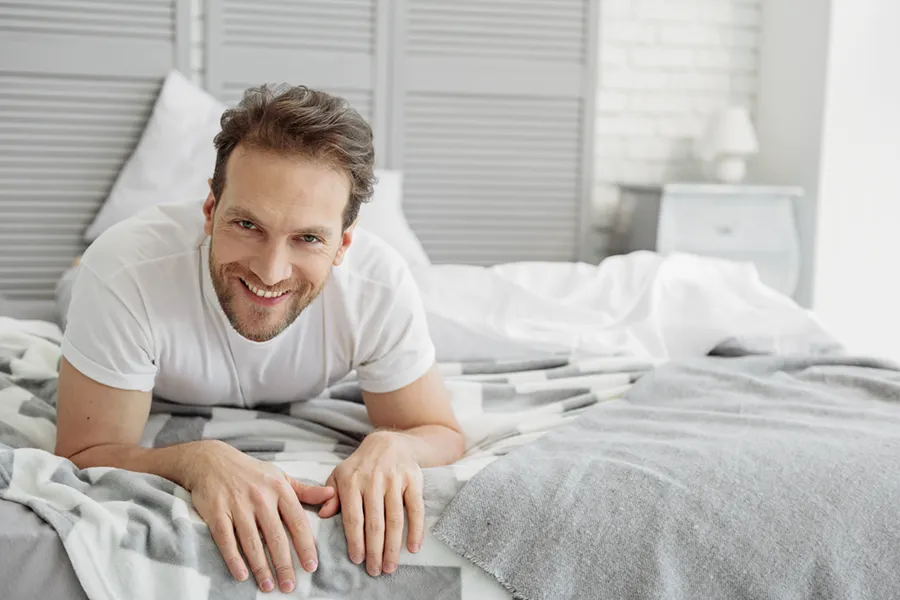Low-Libido-in-Men-Doctor A dirty-blonde haired man lays on his stomach in bed smiling. Schedule treatment for low libido in men from Frank Lanzisera, D.C. in Tampa Bay Metro.