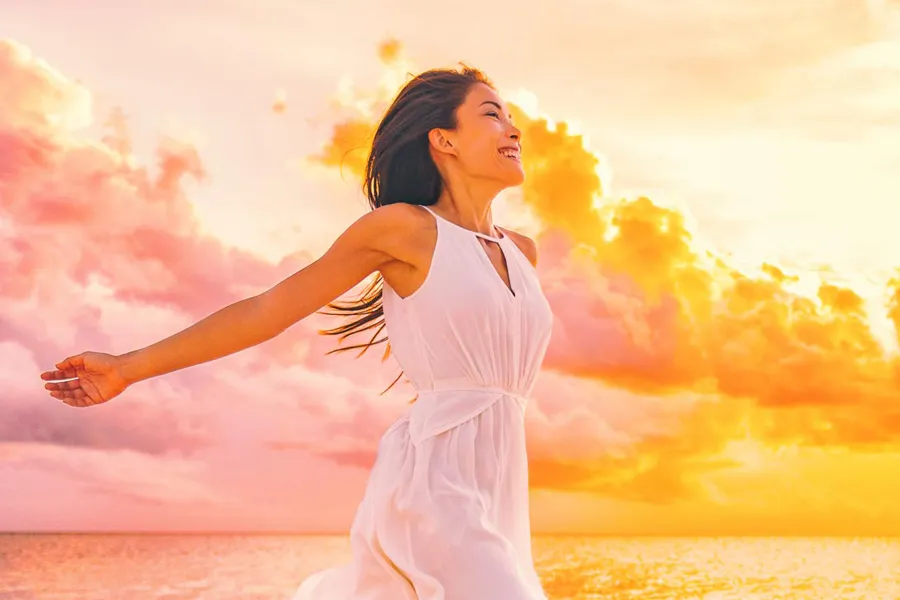 Myers-Cocktail-Clinic A woman in a thin white dress stretches out her arms joyously on the beach at sunrise. Get the Myers Cocktail IV treatment from Frank Lanzisera, D.C. in Tampa Bay Metro.