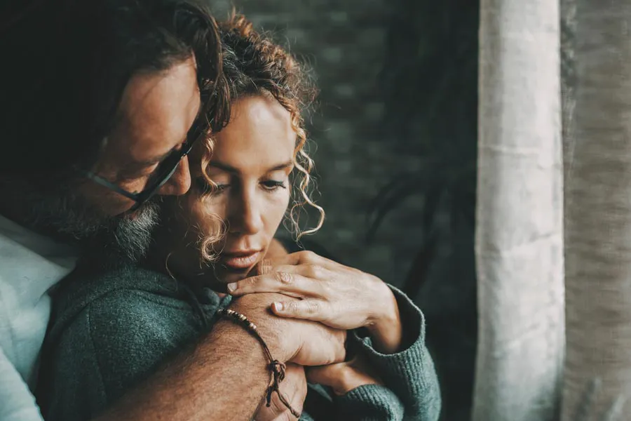 Neurodegenerative-Disorders-Therapy A man embraces a woman from behind in a dimly lit room, their somber expressions showing concerns about a neurodegenerative disease they will get treated by Frank Lanzisera, D.C. in Tampa Bay Metro.