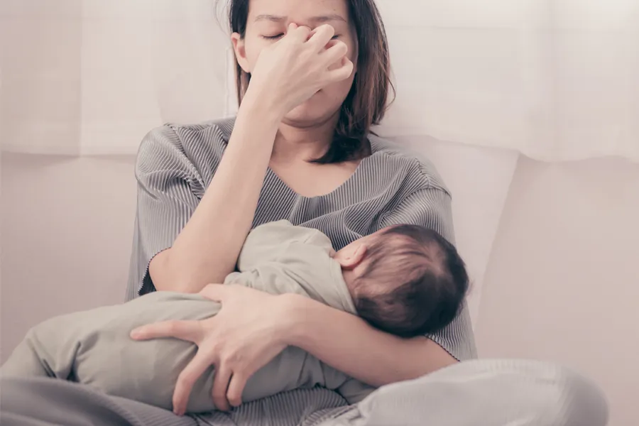 Postpartum-Hormone-Imbalance-Clinic A woman nursing an infant on couch rubs her eyes with exhaustion. Get treatment for postpartum hormone imbalance from Frank Lanzisera, D.C. in Tampa Bay Metro.