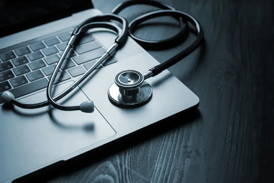 Telemedicine-Doctor An open laptop with a stethoscope lying on it on a wooden table, symbolizing telemedicine care from Frank Lanzisera, D.C. in Tampa Bay Metro.