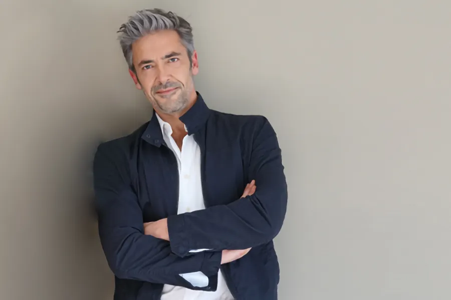 Testosterone-Low-T-Solutionsn-Clinic A middle-aged man in a white shirt and dark blue jacket leans against a gray wall smiling. Get testosterone for Low T from Frank Lanzisera, D.C. in Tampa Bay Metro.