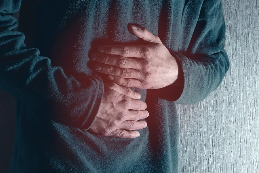 Ulcerative-Colitis-Clinic Close-up of the midsection of a man in a green sweater clutching his gut in pain. Get treatment for Ulcerative Colitis from Frank Lanzisera, D.C. in Tampa Bay Metro.