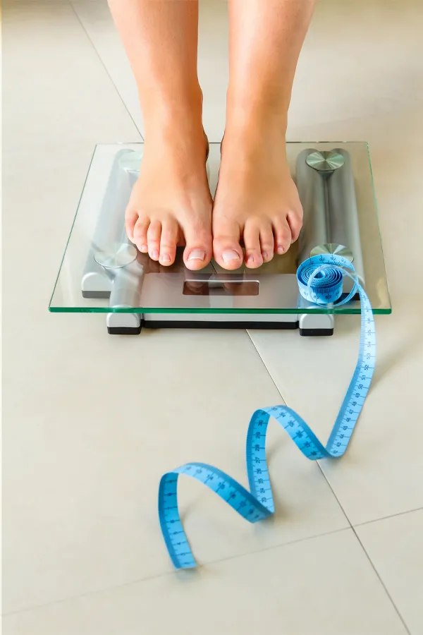 Weight-Loss-Resistance-Treatment Close-up of a woman's feet standing on a scale, with measuring tape by her toes, getting treatment for weight loss resistance from Frank Lanzisera, D.C. in Tampa Bay Metro.